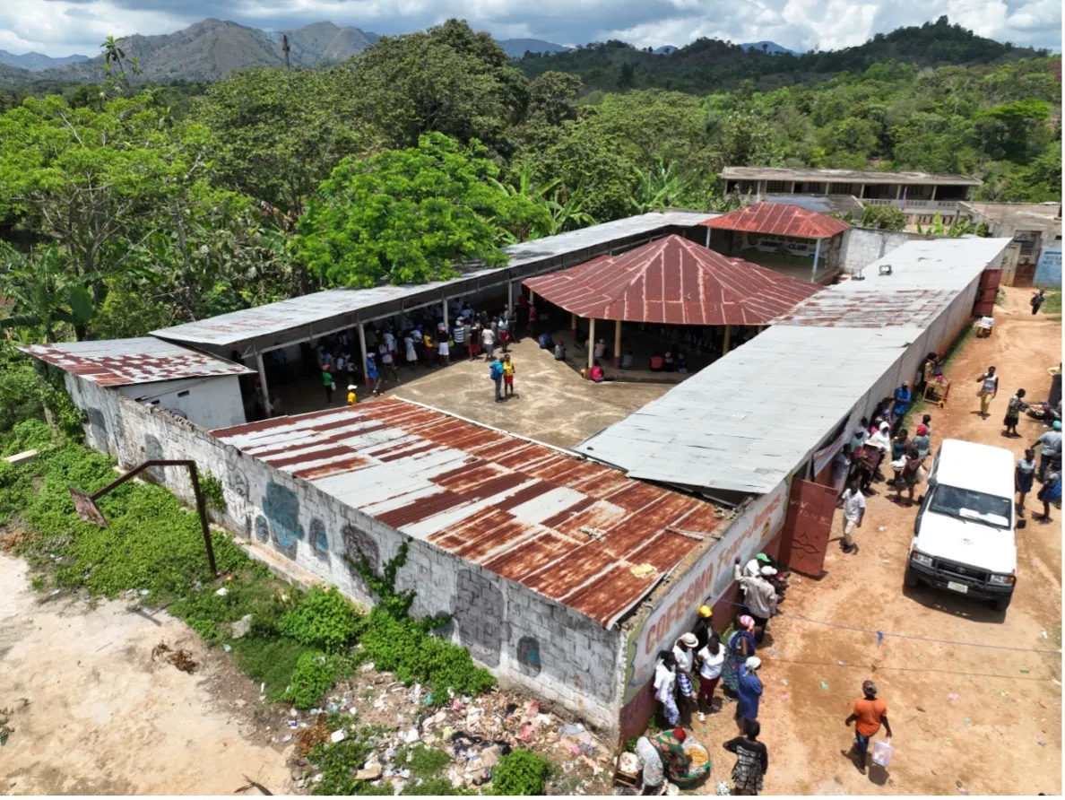 Photo taken from an elevated angle of a tin-roofed, cinder-block complex of buildings with people and vehicles.