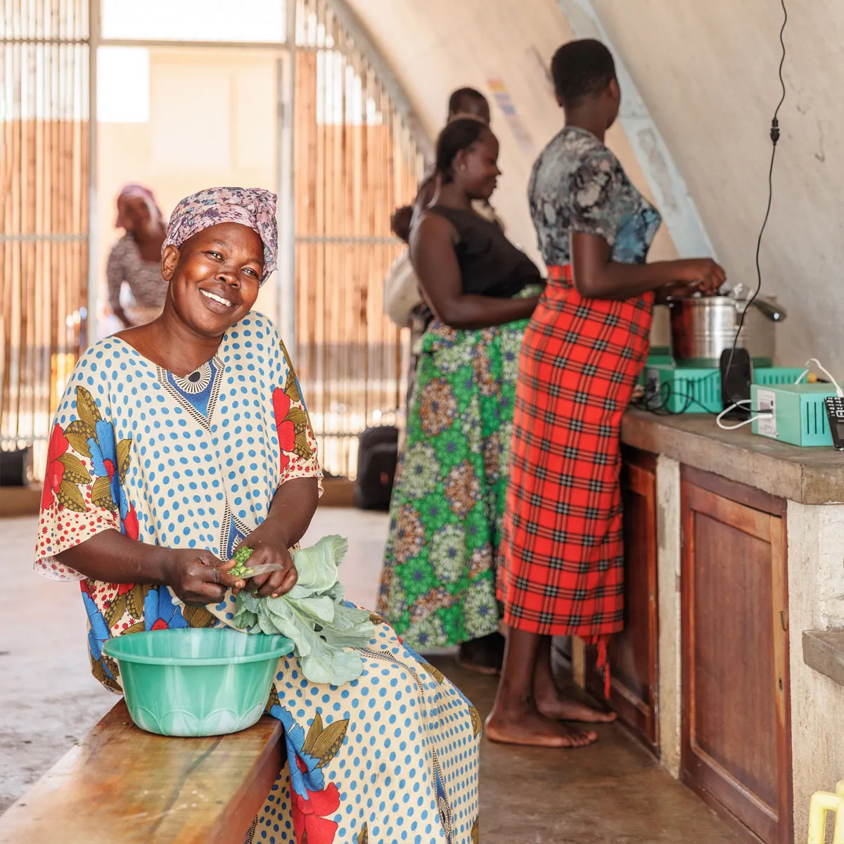 A woman sits on a bench and smiles while cutting produce.
