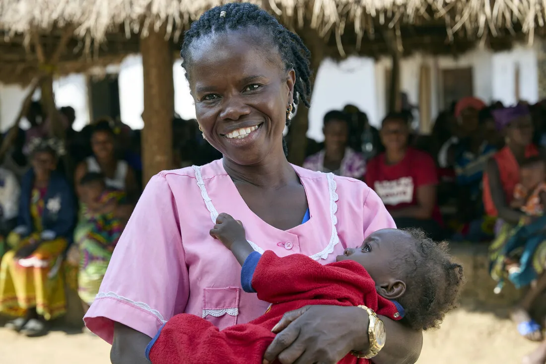 A woman in pink dress holding a baby.